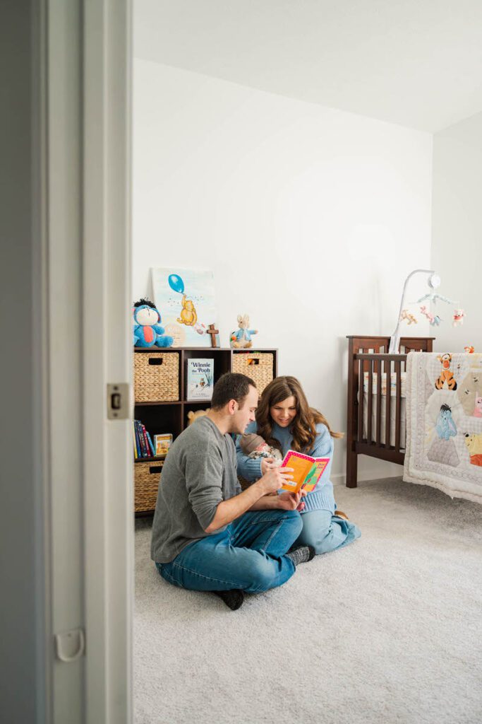 A mom and dad sit on nursery floor and read to their new baby.