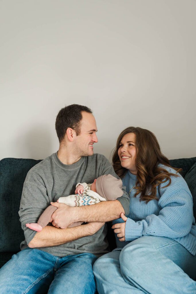A family snuggles up with new baby on a couch.