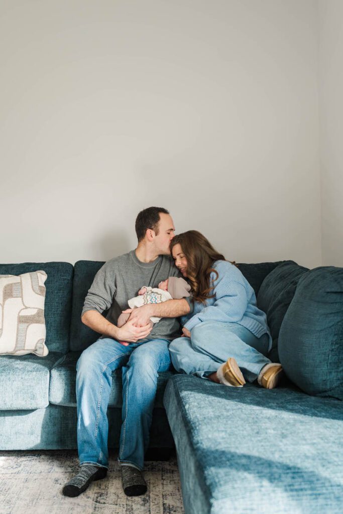A family with a new baby snuggles on a couch.