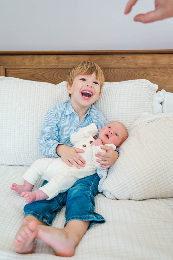 Big brother laughs while holding baby during Louisville in-home newborn session.