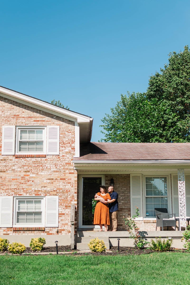 A family poses on their front porch with their newborn baby. Louisville In-Home Newborn Photographer Michelle Bordenkircher Photography.