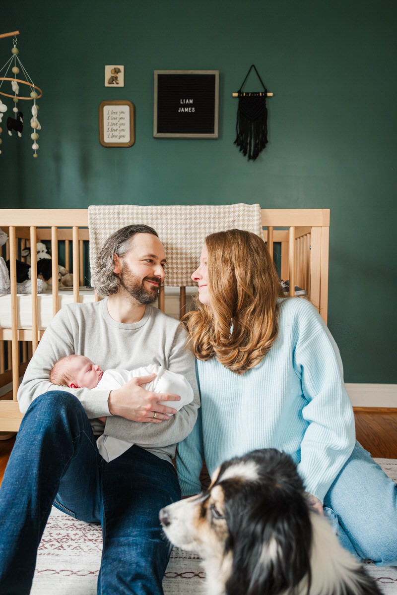A new mom and dad sit with their new baby in the nursery. Louisville In Home Newborn Session Photos by Michelle Bordenkircher Photography