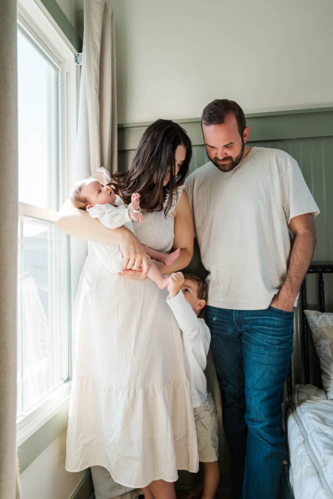 A family stands near a window during their Louisville In-Home Family Photography Session. Photos by Michelle Bordenkircher Photography.