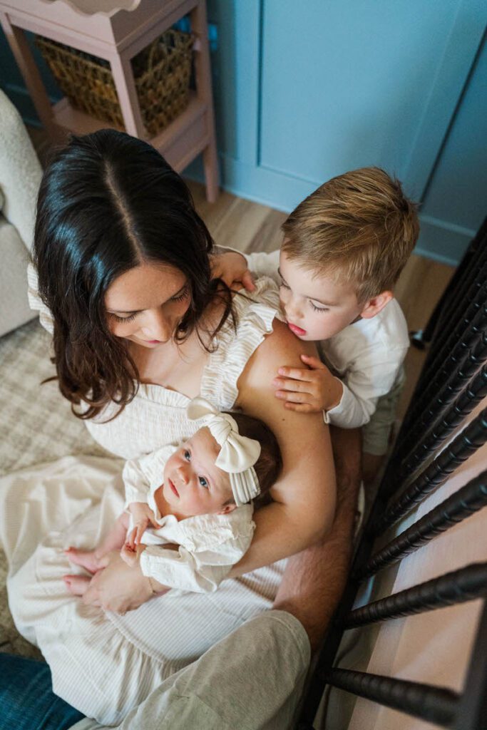 A big brother looks at his mom and little sister during their Louisville In-Home Family Photography Session. Photos by Michelle Bordenkircher Photography.