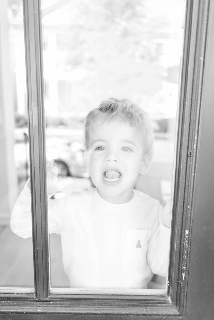 A little one looks through a window during a Louisville In-Home Family Photography Session. Photos by Michelle Bordenkircher Photography.