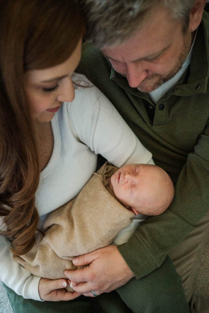 A mom and dad smile at their new baby boy during their Louisville In-Home newborn session Photos by Michelle Bordenkircher Photography